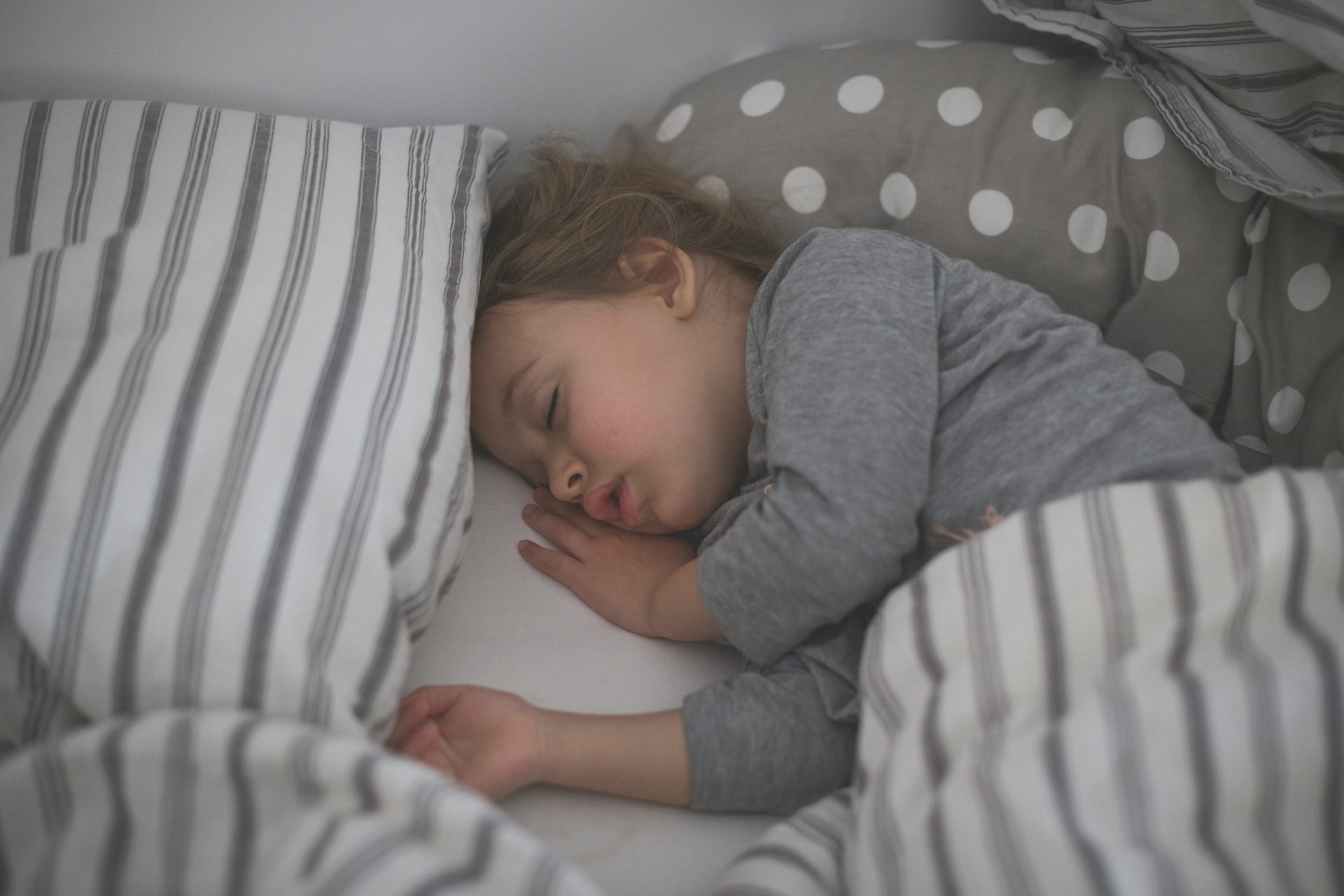 baby in gray long sleeve shirt lying on white and black stripe bed
