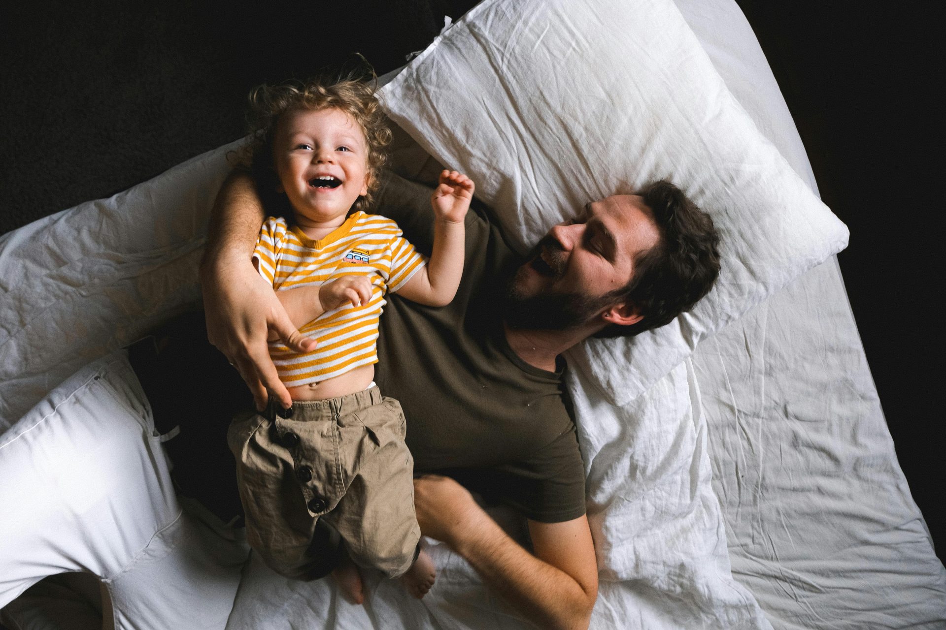 A joyful moment of a father and son laughing together in bed, capturing family happiness.