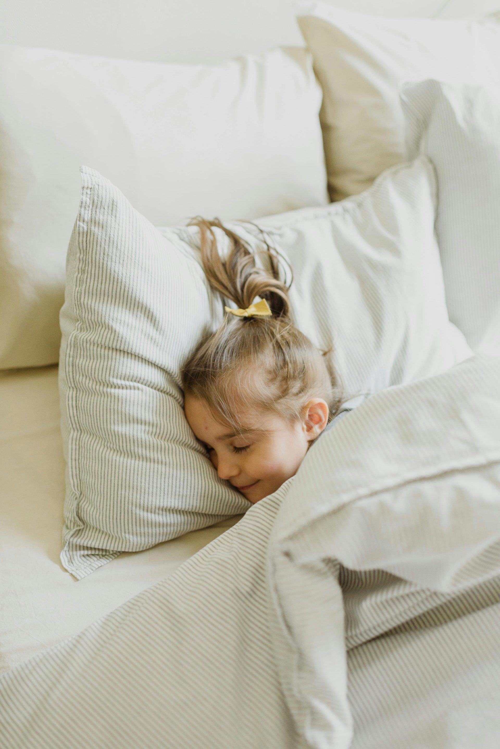 A peacefully sleeping child nestled in white pillows and a warm blanket.