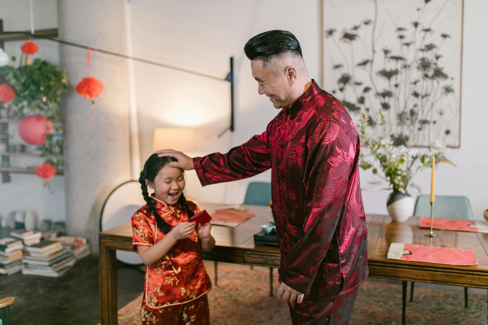 A joyful moment of a grandfather giving a red envelope to his granddaughter dressed in traditional Chinese clothing indoors.