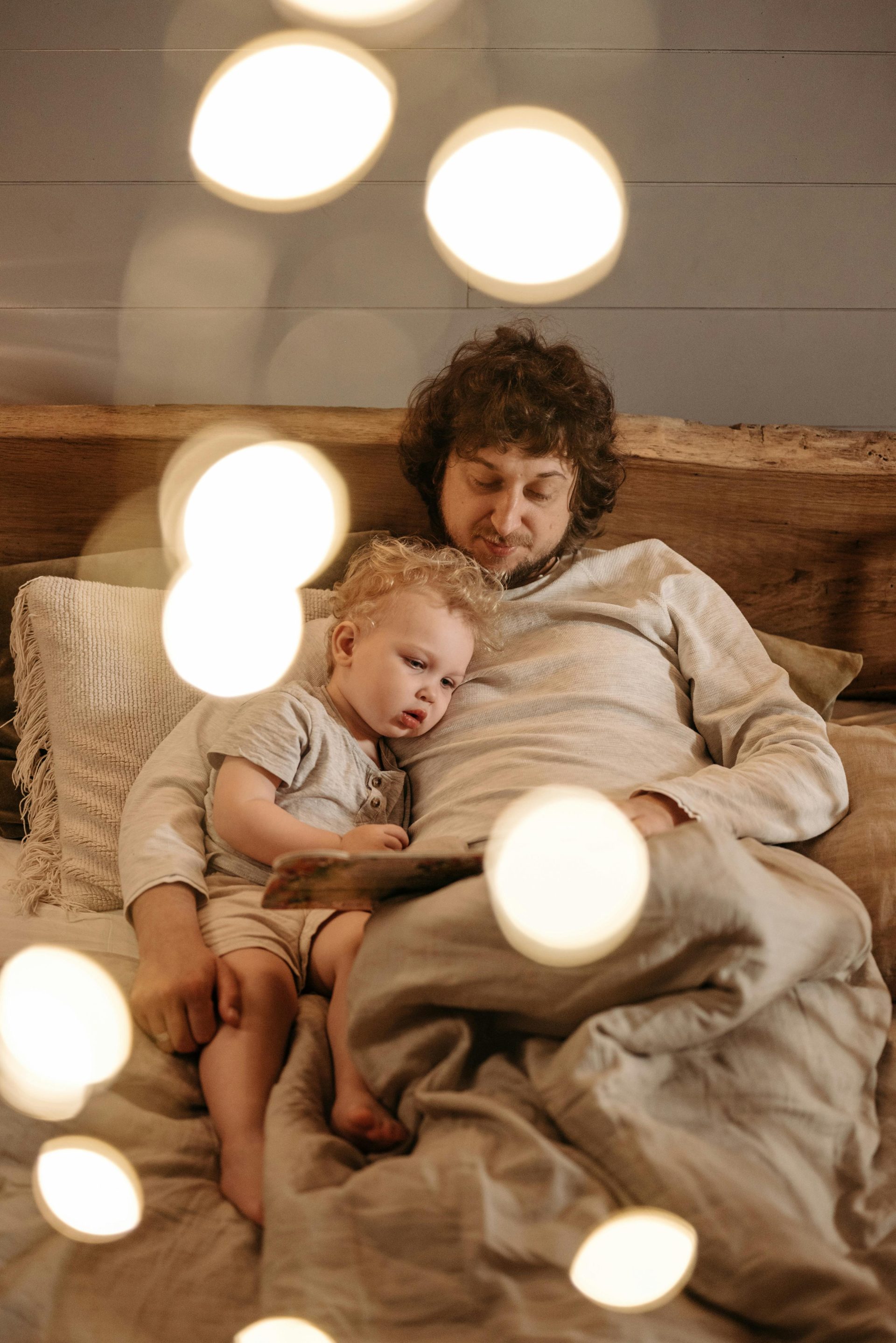 A father and child enjoy a bedtime story in a warmly lit bedroom with soft bokeh lighting.